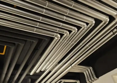 Parallel geführte, metallummantelte Rohrleitungen unter einer Hallendecke.