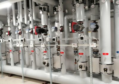 Gedämmte Heizungsleitungen mit Pumpen und Verteilsystem in einem Technikraum.