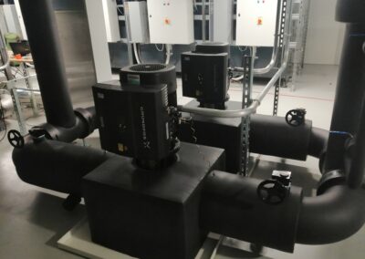 Umwälzpumpen mit schwarz isolierten Rohrleitungen in einer technischen Anlage.