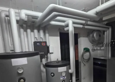 Isolierte Heizungsleitungen und Warmwasserspeicher in einem Technikraum.