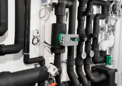 Schwarz isolierte Kälte- und Heizleitungen mit Armaturen in einem Technikraum.